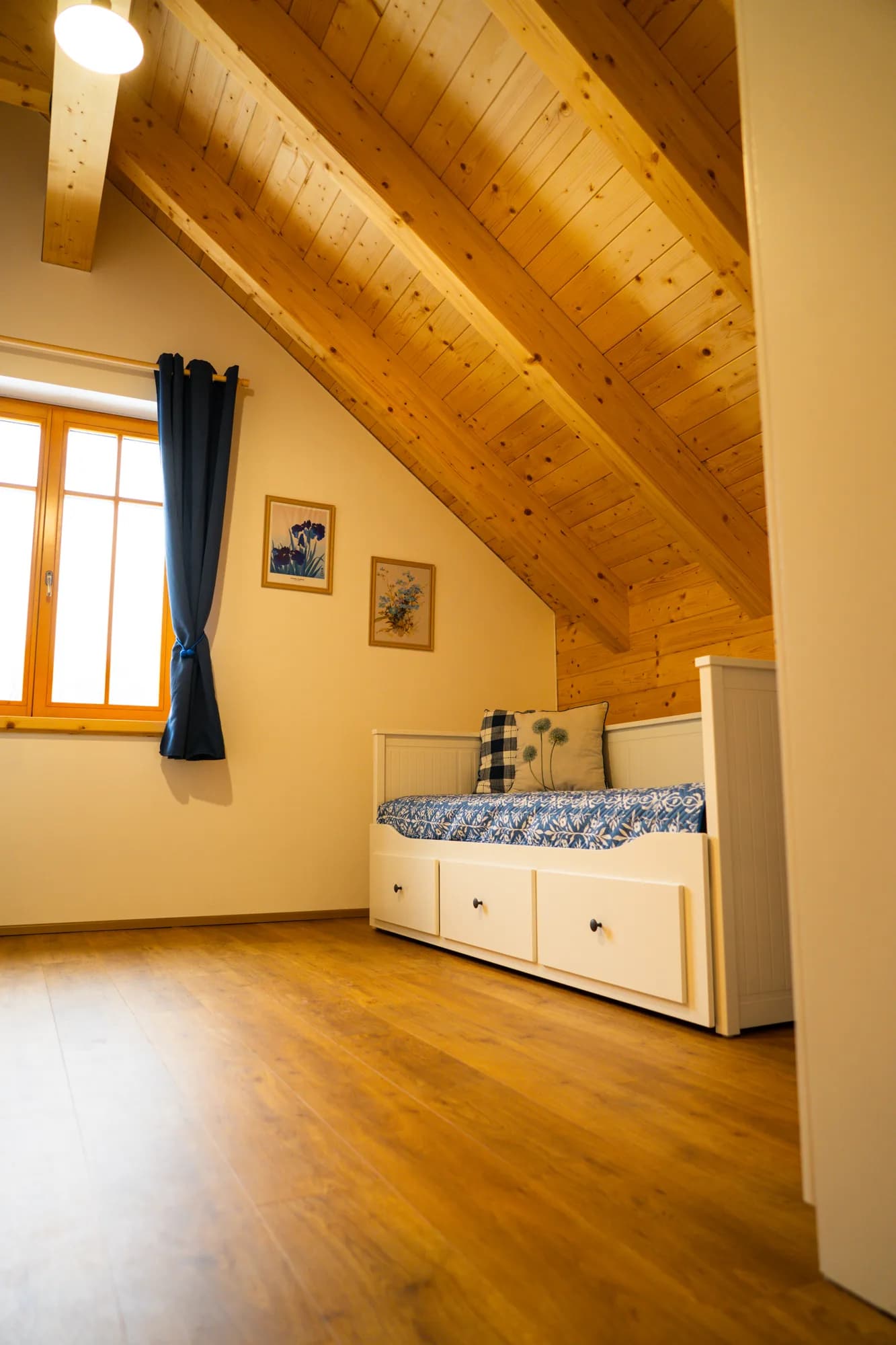 Druhá podkrovní ložnice s rozkládací postelí a šikmým dřevěným stropem